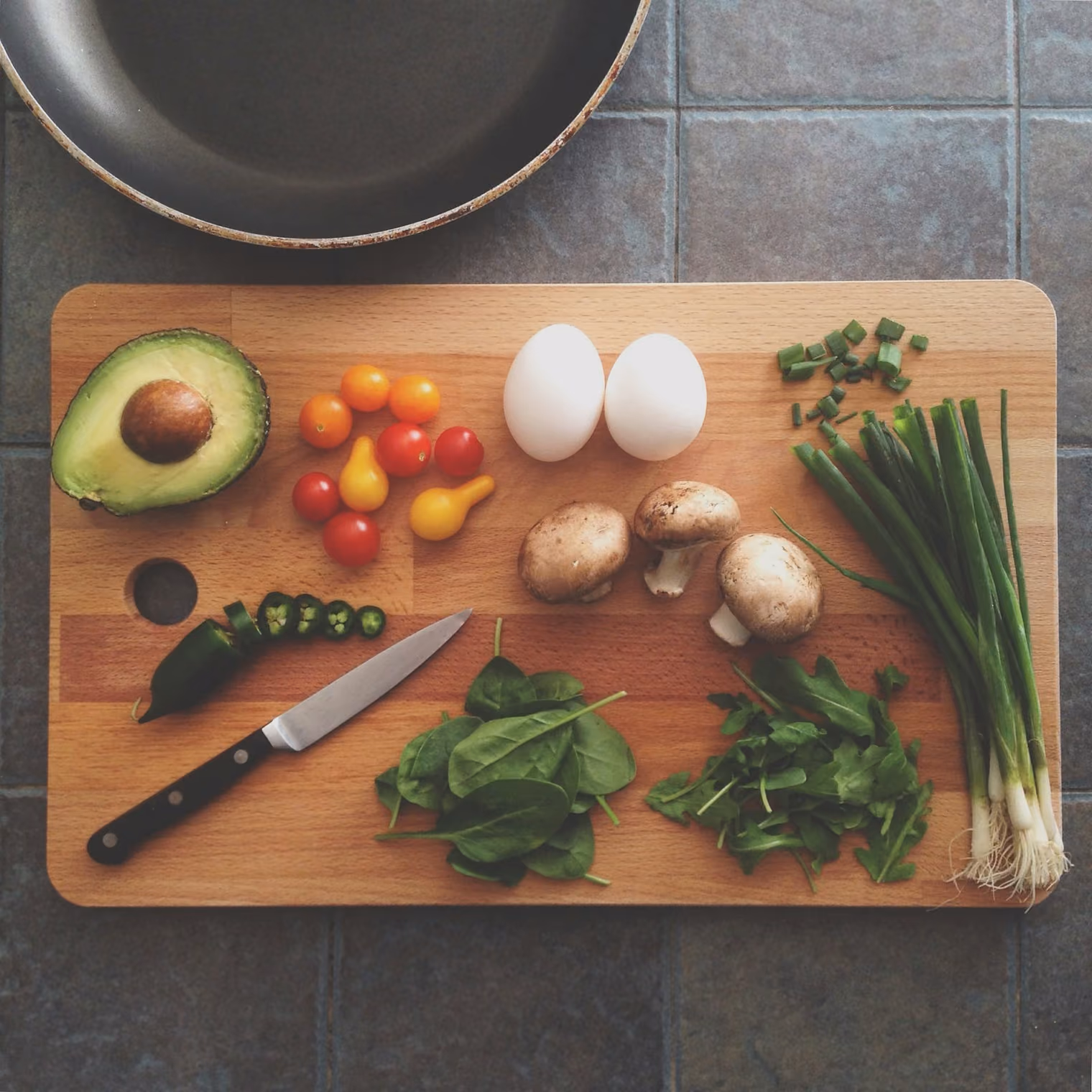Avocado, Eier, Pilze und Tomaten auf einem Holzbrett