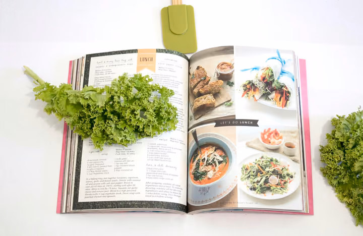 Aufgeschlagenes Kochbuch mit Rezeptfotos neben frischem Grünkohl