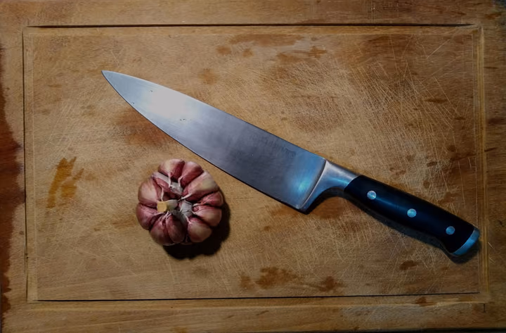 Kochmesser mit schwarzem Griff neben einer Knoblauchknolle auf einem Holzbrett